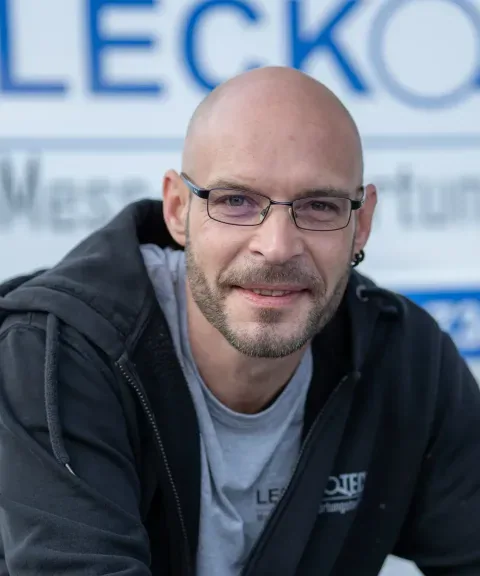 Mitarbeiter von LECKOTECH lächelt für ein Porträtfoto vor dem Firmenbanner